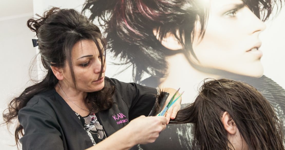 Una parrucchiera del salone, con la divisa Katia Hair Studio, taglia i capelli bagnati di una cliente